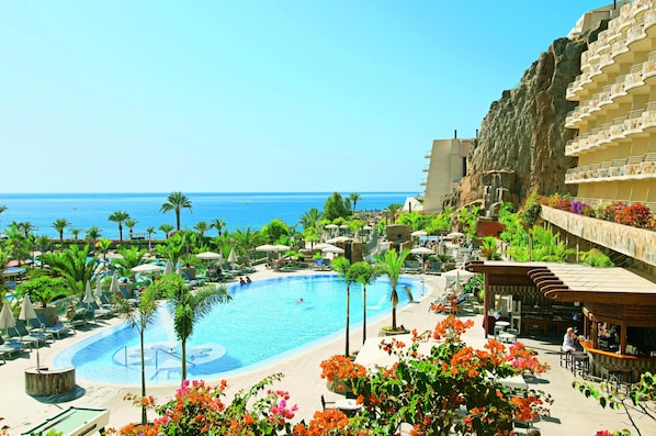 Un resort con una piscina grande, sillas de descanso y vistas al océano.