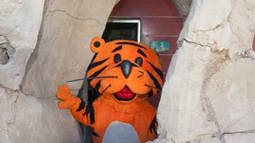 A tiger mascot in a cave-like structure with a sign reading "Kids Club" in the background.