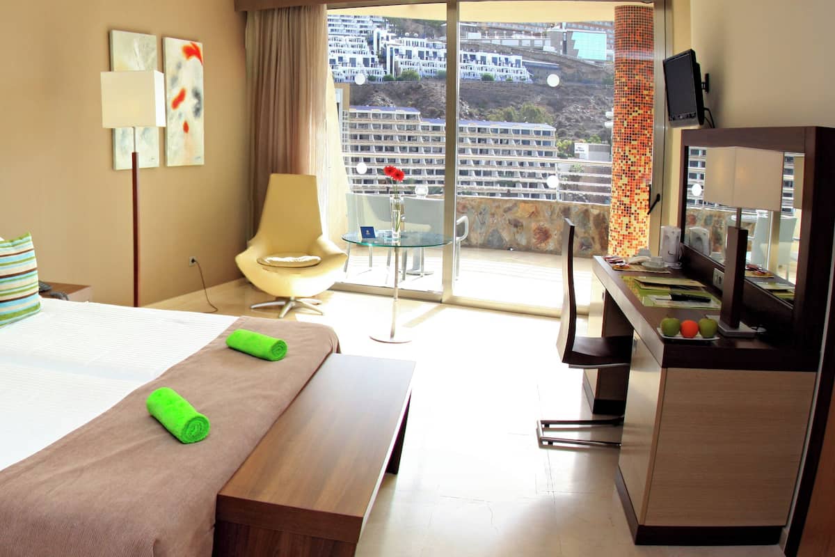 A hotel room with a large bed, a desk, a chair, and a view of the city.