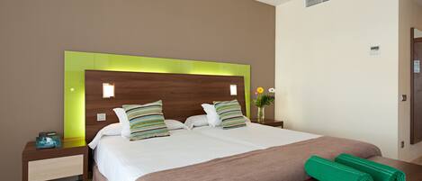 A modern hotel room with a large bed, a bedside table, a nightstand, and a green towel on the side table.