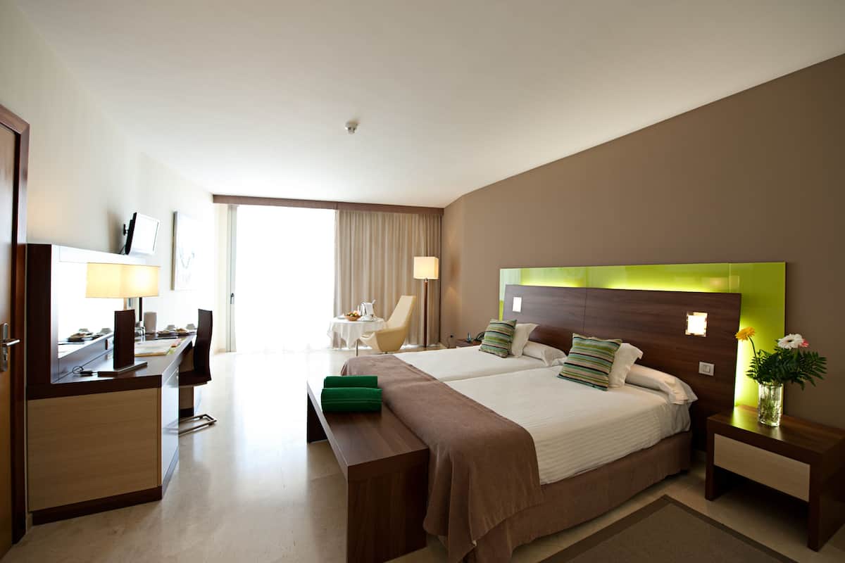 A hotel room with two beds, a desk, a chair, a TV, and a window with curtains.