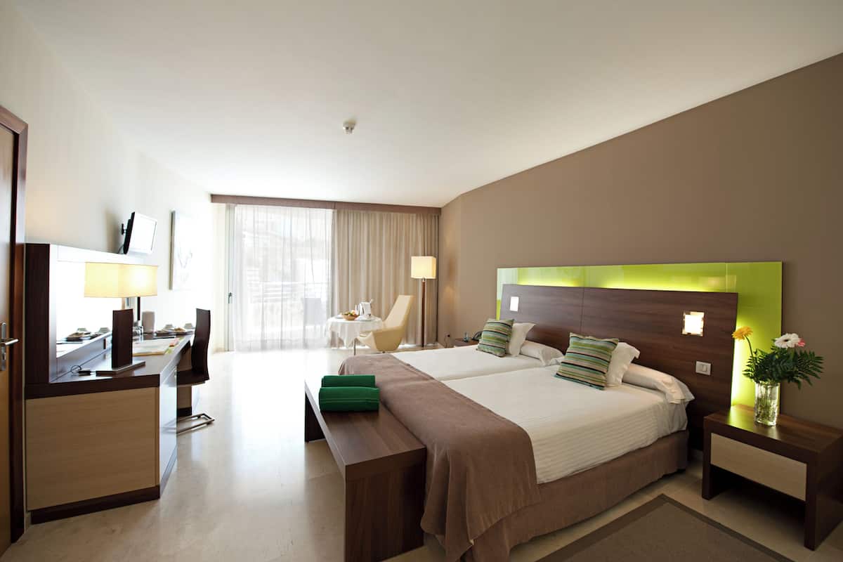 A hotel room with two beds, a desk, a chair, a TV, and a window with curtains.