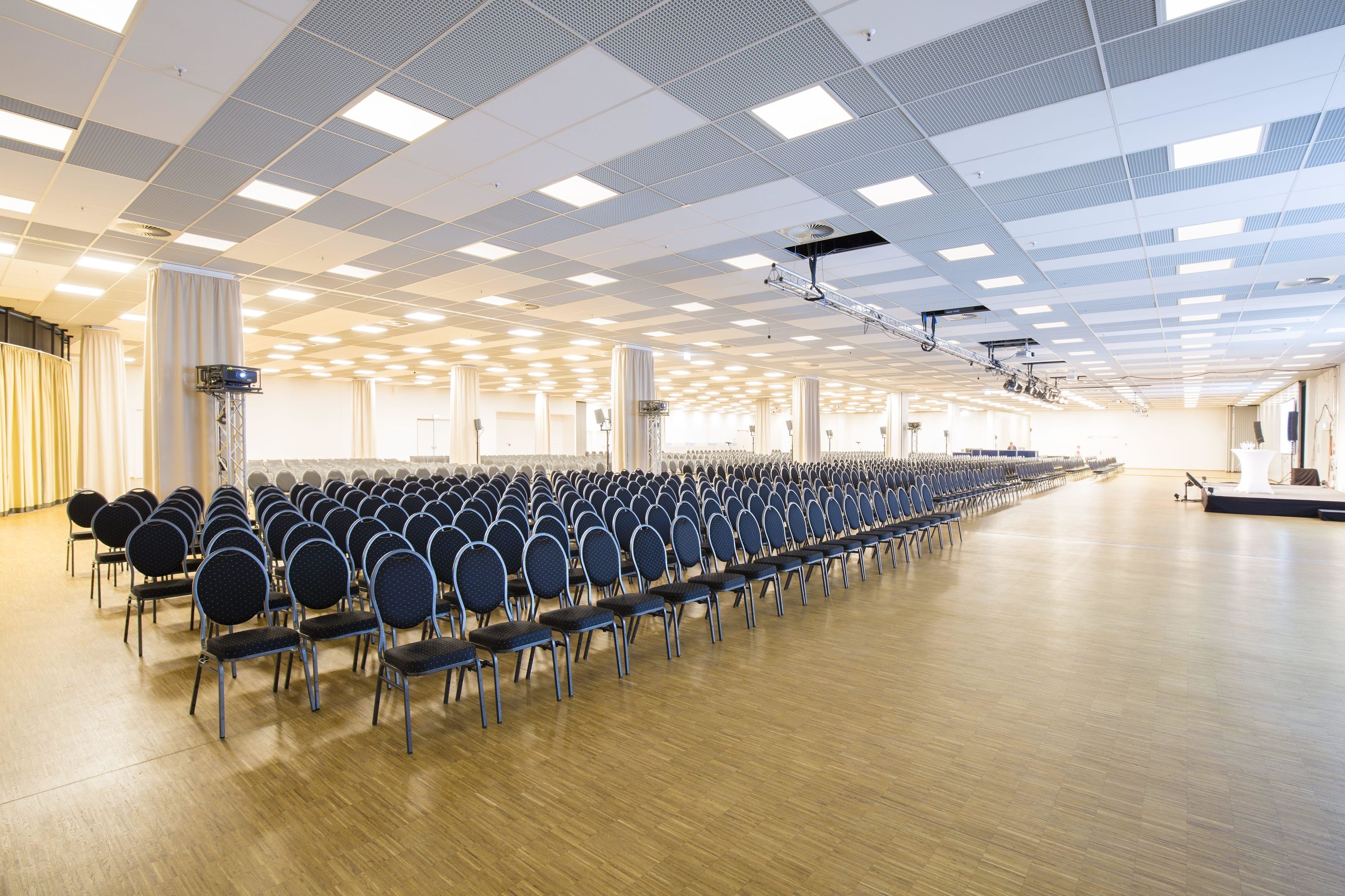 Une grande salle avec des rangées de chaises et une scène.