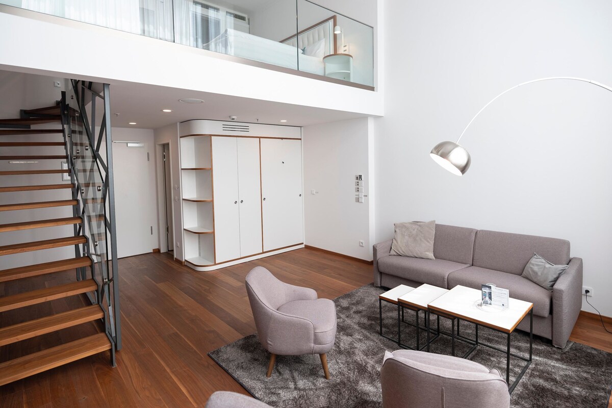 A modern living room with a staircase, a grey sofa, a coffee table, and a wardrobe.