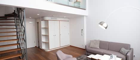 A modern living room with a staircase, a grey sofa, a coffee table, and a wardrobe.