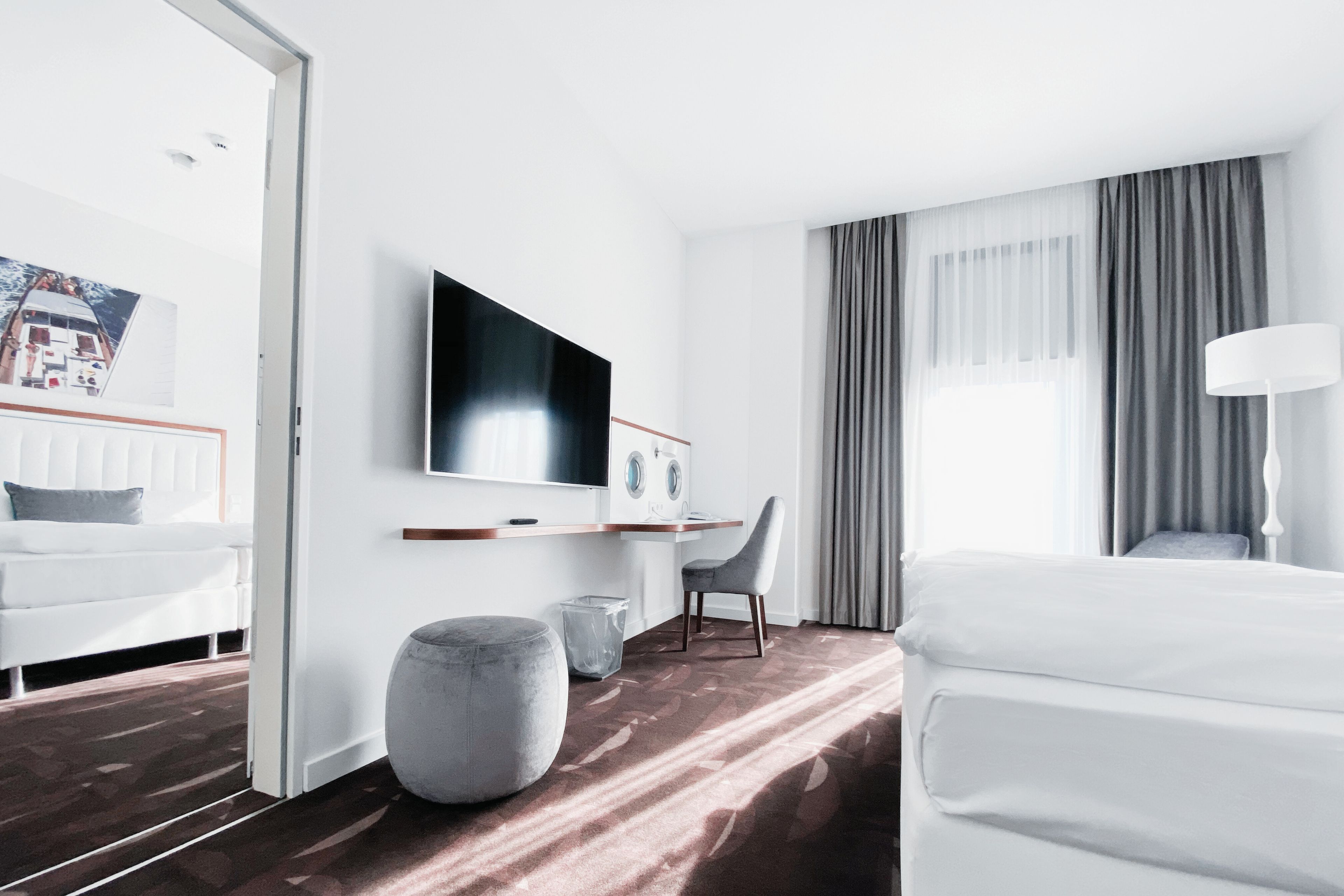Ein modernes Hotelzimmer mit einem Bett, einem Schreibtisch, einem Fernseher und einem großen Fenster mit Vorhängen.