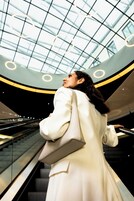A person ascending an escalator in a modern building with a glass ceiling and circular light fixtures.