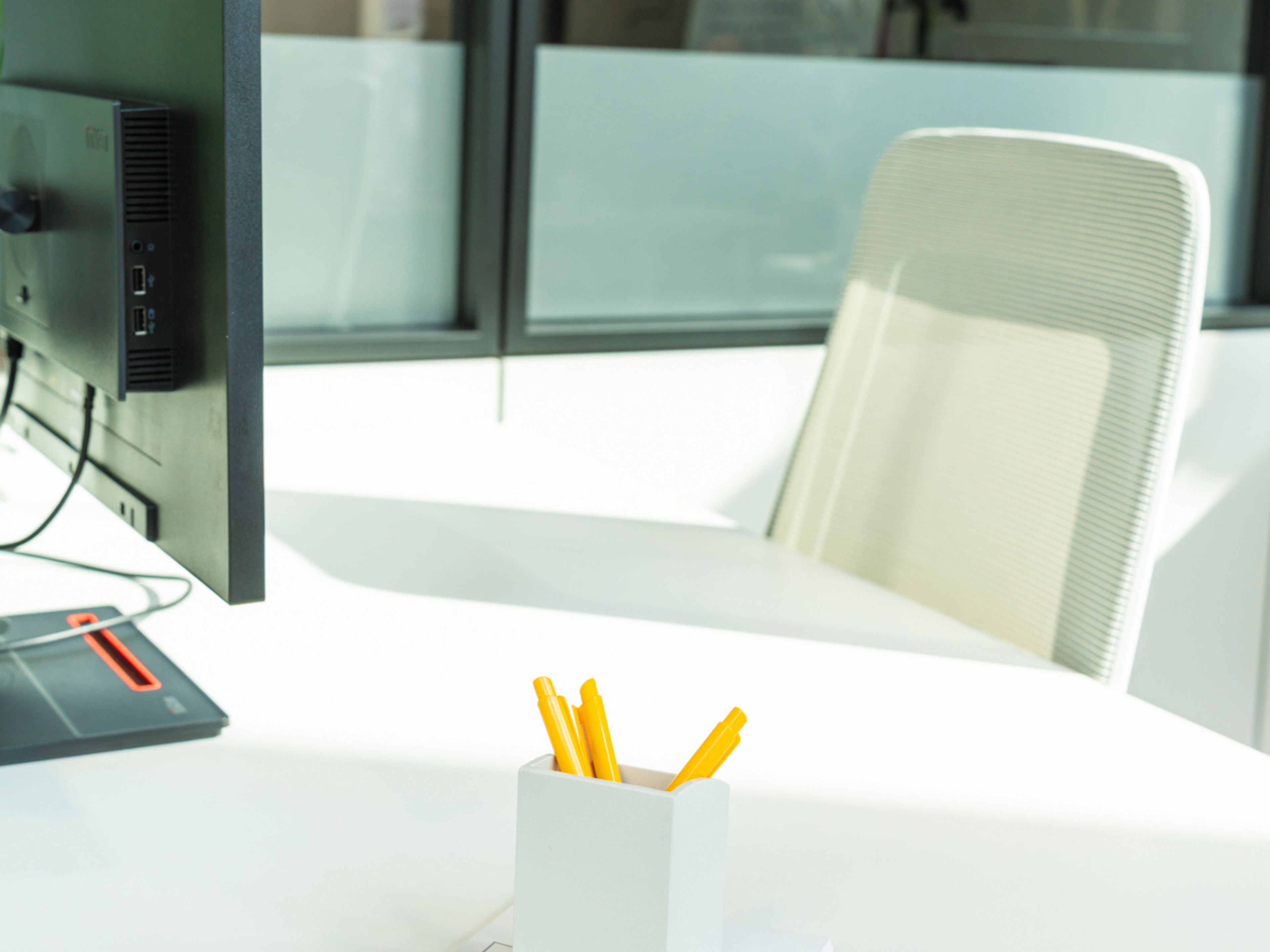 Een bureau met een computerscherm, een stekkerdoos en een witte stoel.