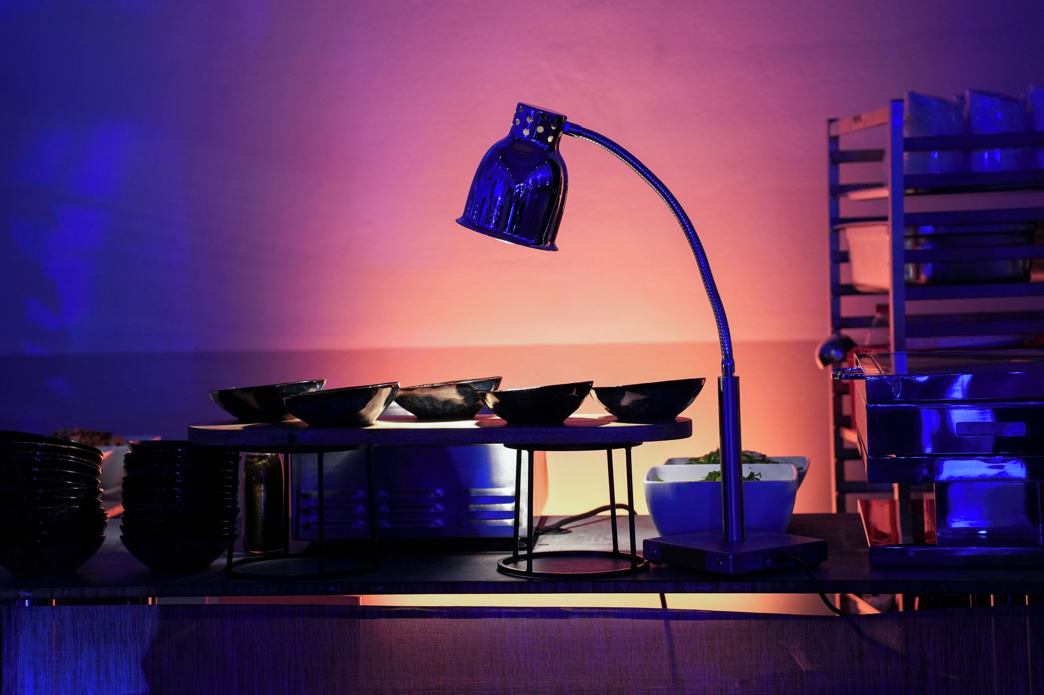 A kitchen with a blue lamp, a metal rack, and a bowl of greens.