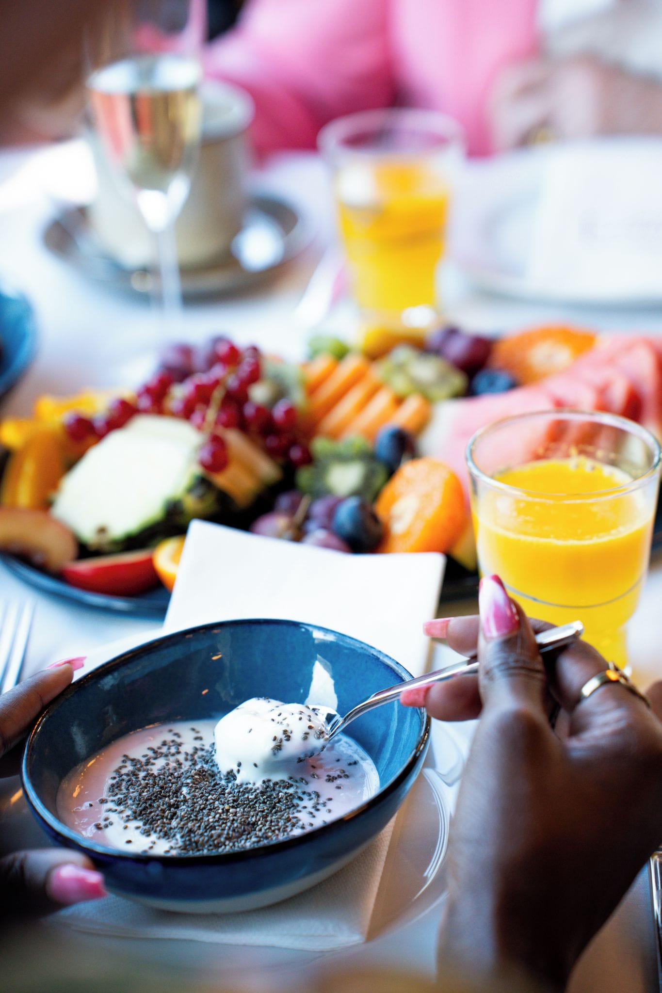 En morgenmadsopsætning med et fad frugt, et glas appelsinjuice og en skål yoghurt med kerner.