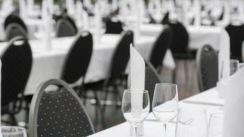 Un'ambientazione da ristorante con tavoli apparecchiati per la cena, caratterizzata da tovaglie bianche, sedie nere e bicchieri trasparenti.
