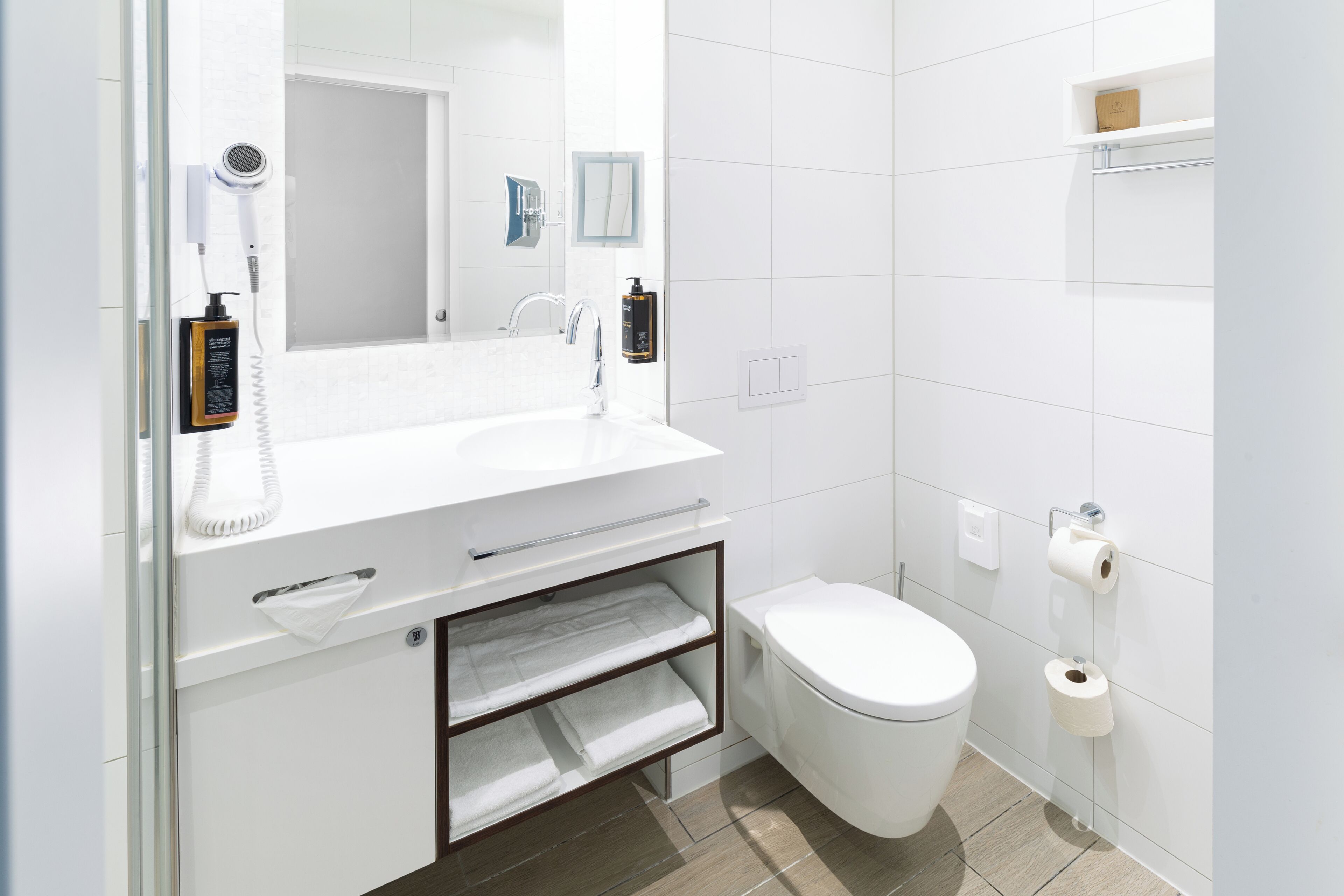 Un baño moderno con un lavabo blanco, un espejo, un inodoro y un perchero para toallas.