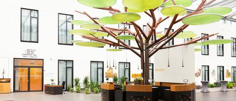 Un área de recepción con una estructura moderna que evoca a un árbol, con elementos circulares verdes, una mesa de recepción y una puerta de cristal.