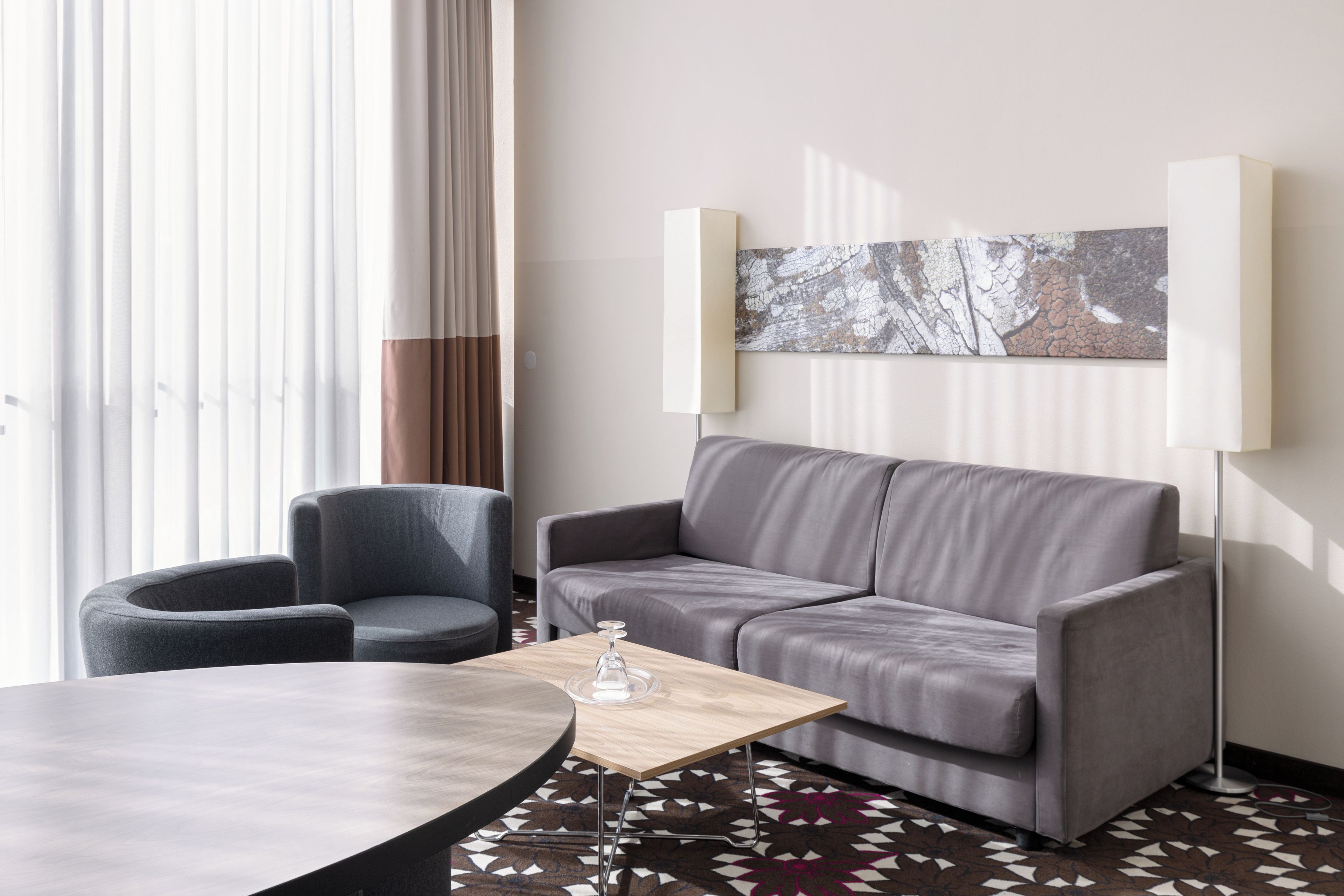 Una habitación de hotel moderna con un sofá gris, una mesa redonda y un piso con diseño.