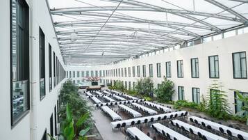 A spacious indoor area with rows of tables and chairs, large windows, and a high ceiling with a metal framework.