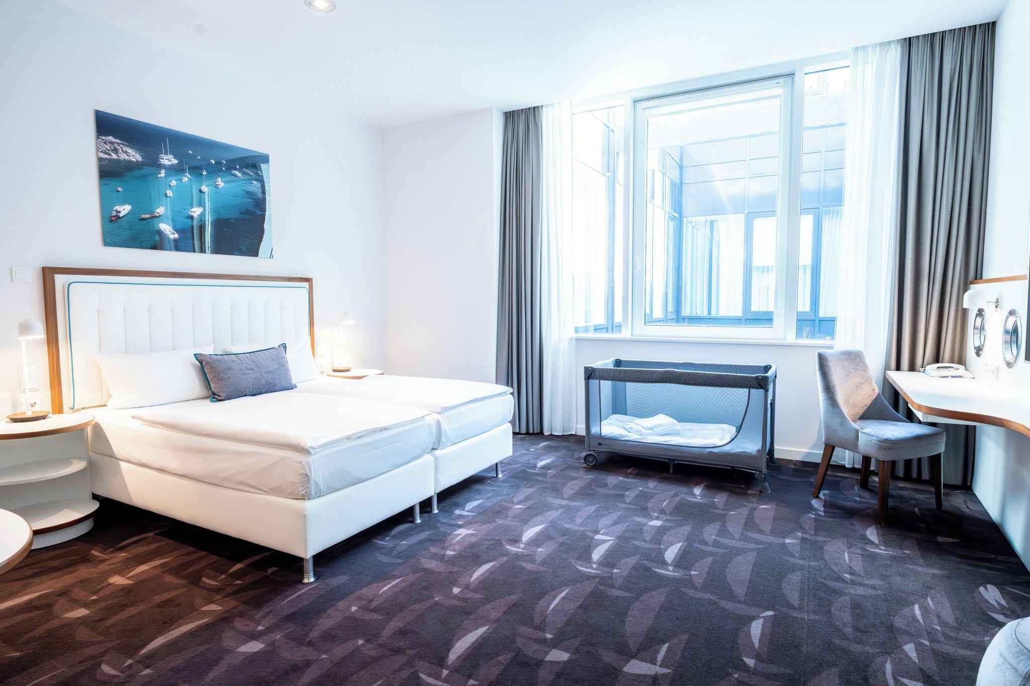 Habitación de hotel con cama, escritorio, silla, ventana y un cuadro en la pared.