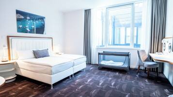 Habitación de hotel con cama, escritorio, silla, ventana y un cuadro en la pared.