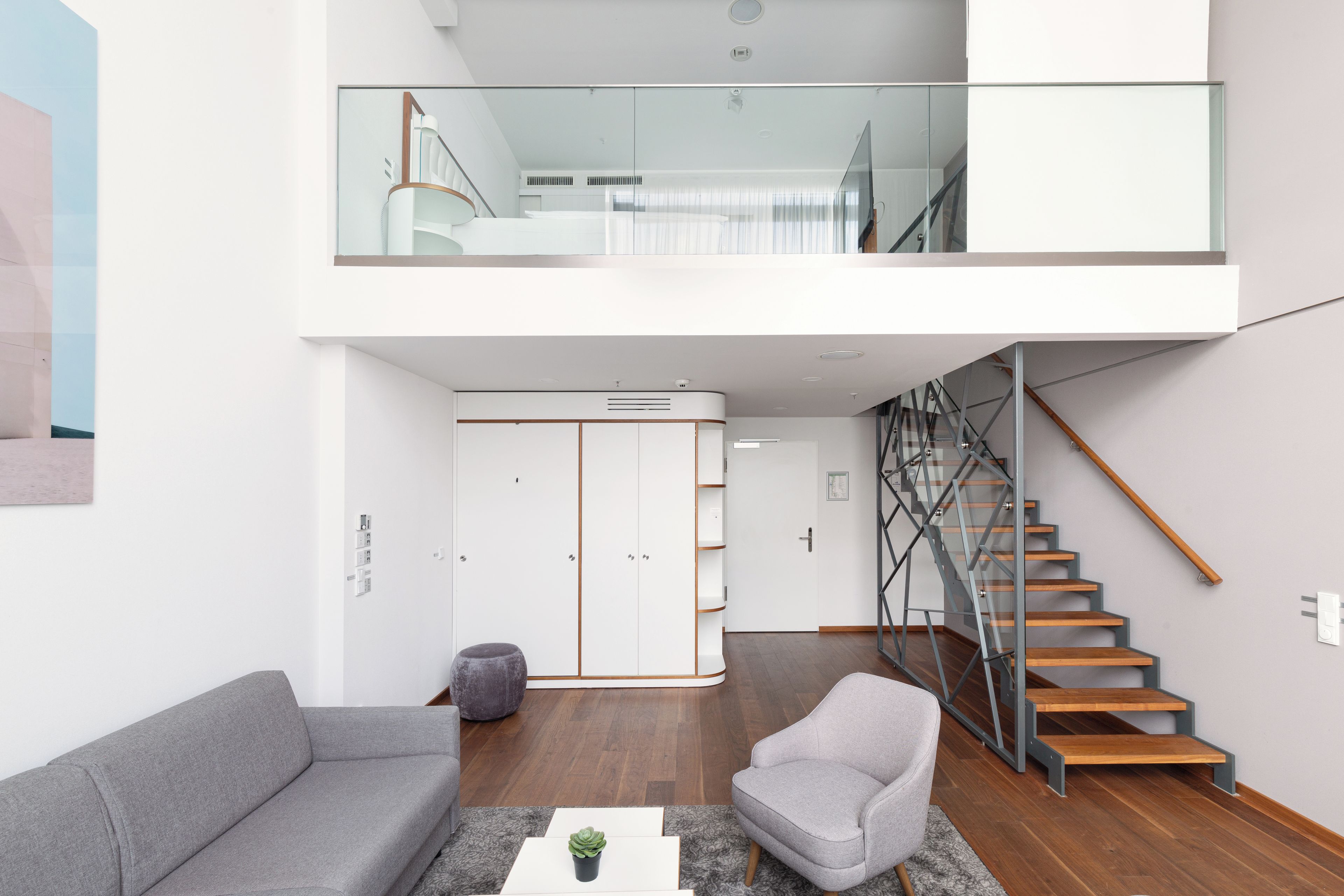 Un salon moderne avec un canapé, un fauteuil et un escalier doté d’une rampe en verre.