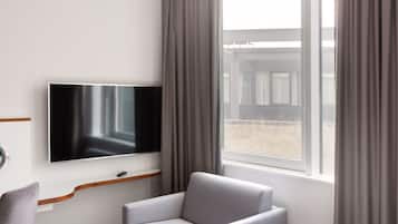A modern room with a flat-screen TV mounted on the wall, a grey armchair, and a window with curtains.
