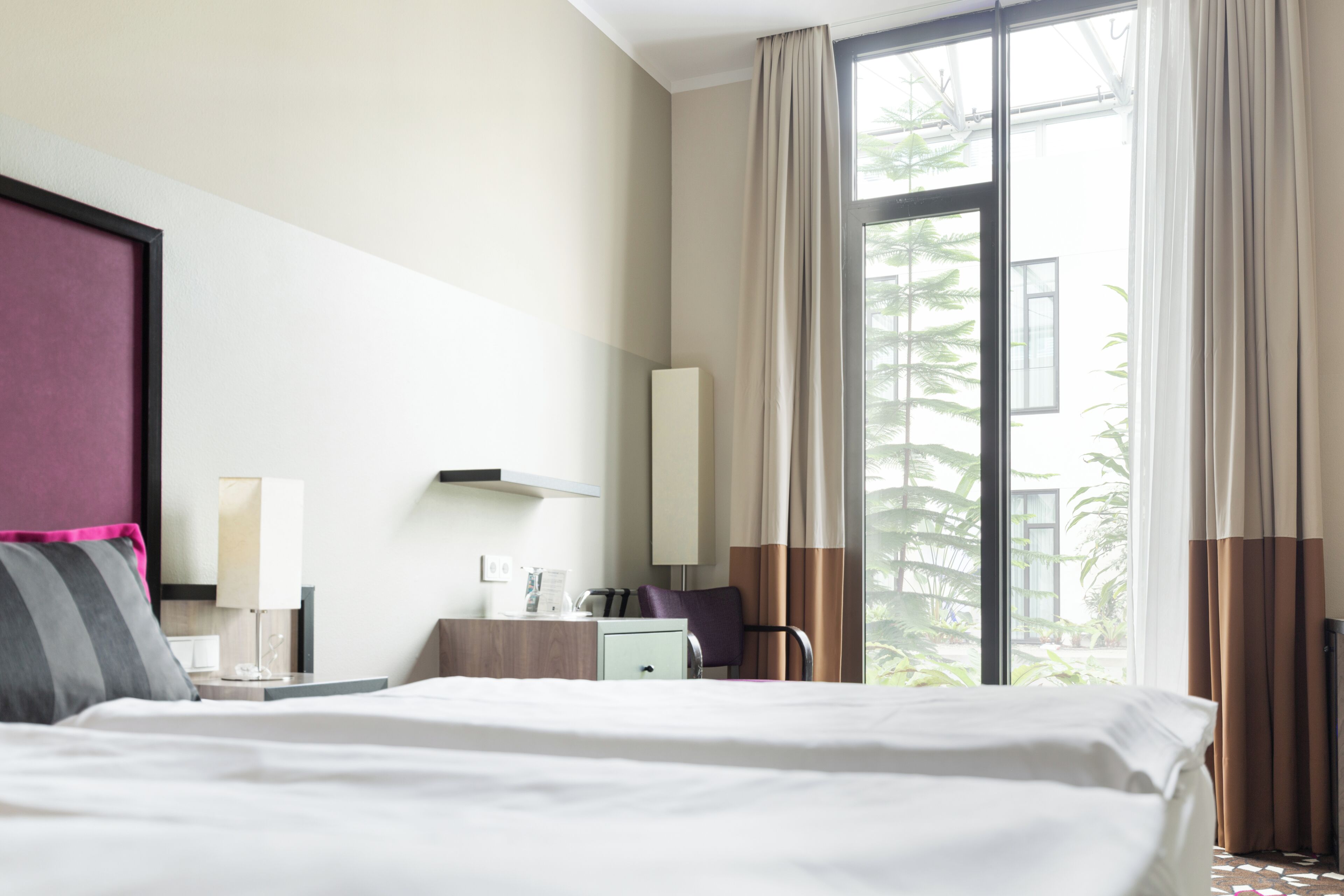 A hotel room with a large bed, a nightstand, a desk, a chair, and a window with curtains.