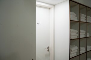 Una puerta blanca con el símbolo de baño, que da a un cuarto con un estante de madera con toallas dobladas.