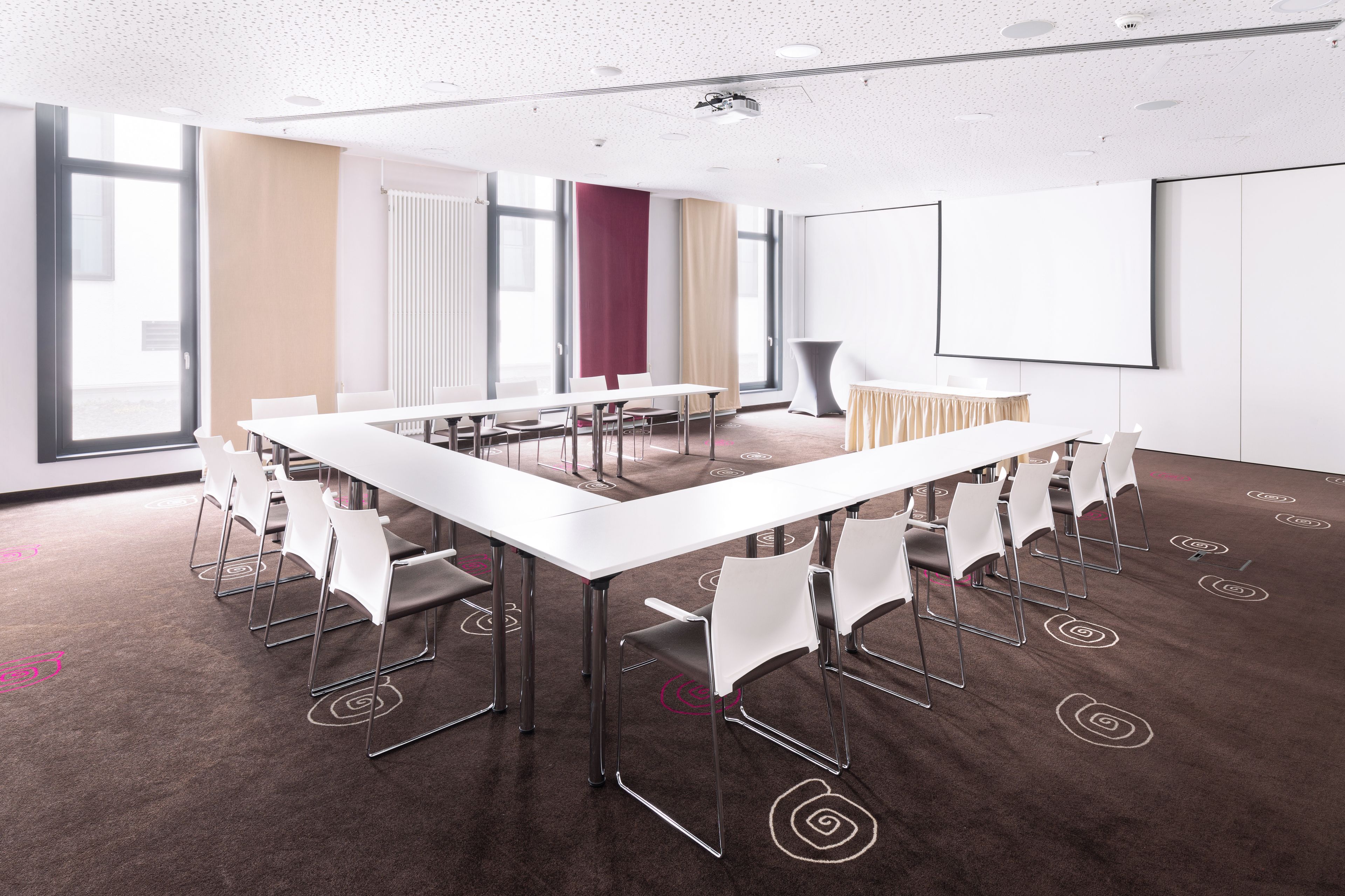 Une salle de conférence équipée d’une grande table, de chaises, d’un projecteur et d’un écran.