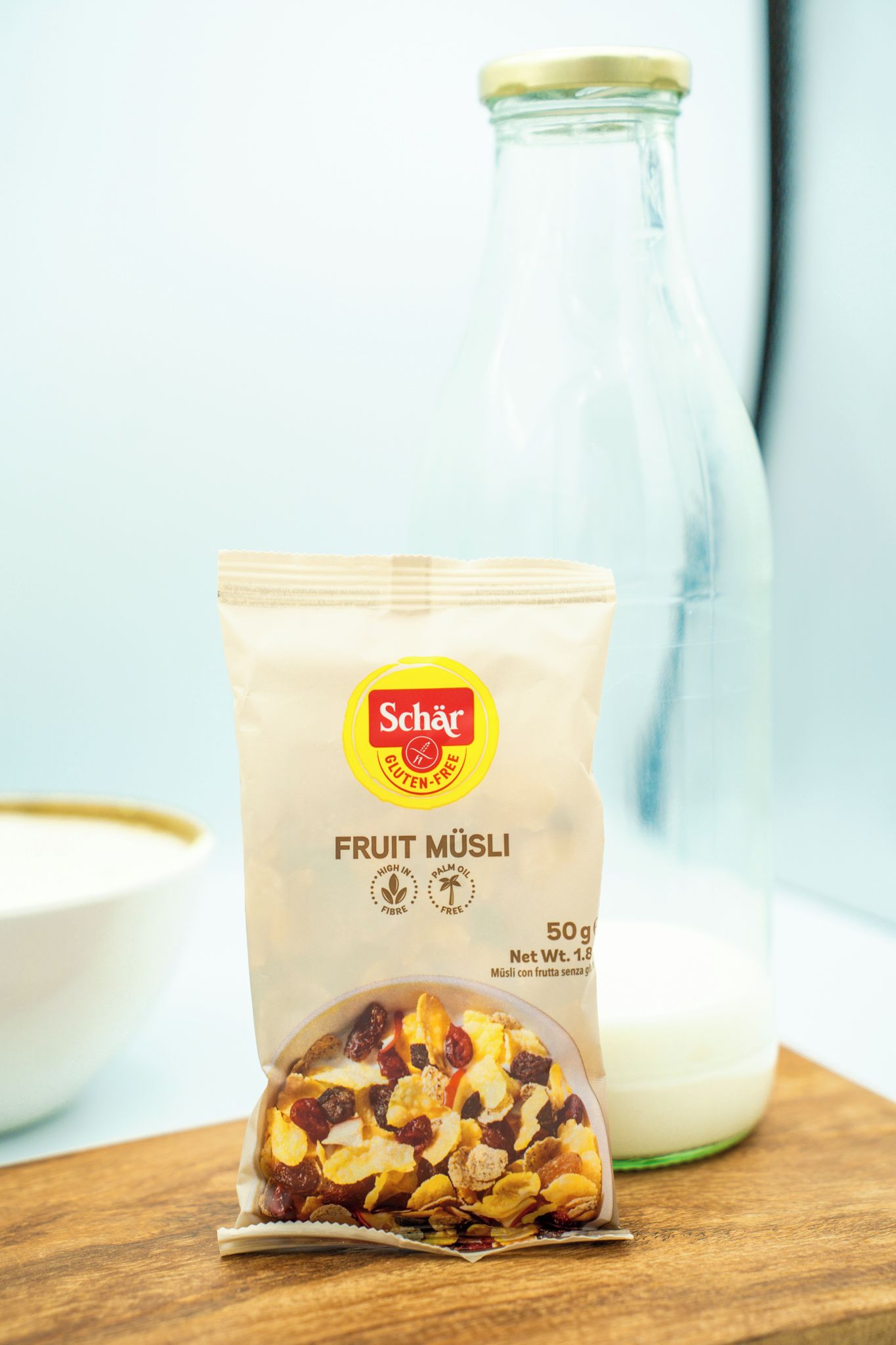 A package of fruit muesli next to a glass bottle of milk on a wooden surface.