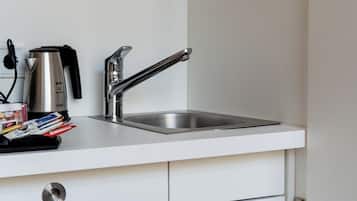 Una cocina con un lavamanos de acero inoxidable, una tetera y un refrigerador.