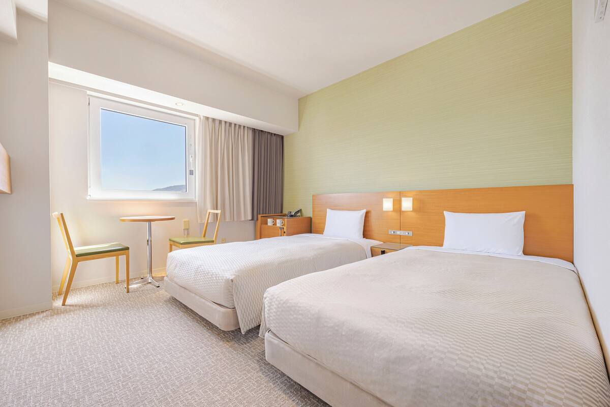 Een hotelkamer met twee bedden, een bureau, een stoel en een raam met gordijnen.