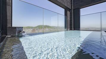 An indoor infinity pool with clear water, surrounded by large windows offering a view of distant hills and buildings.