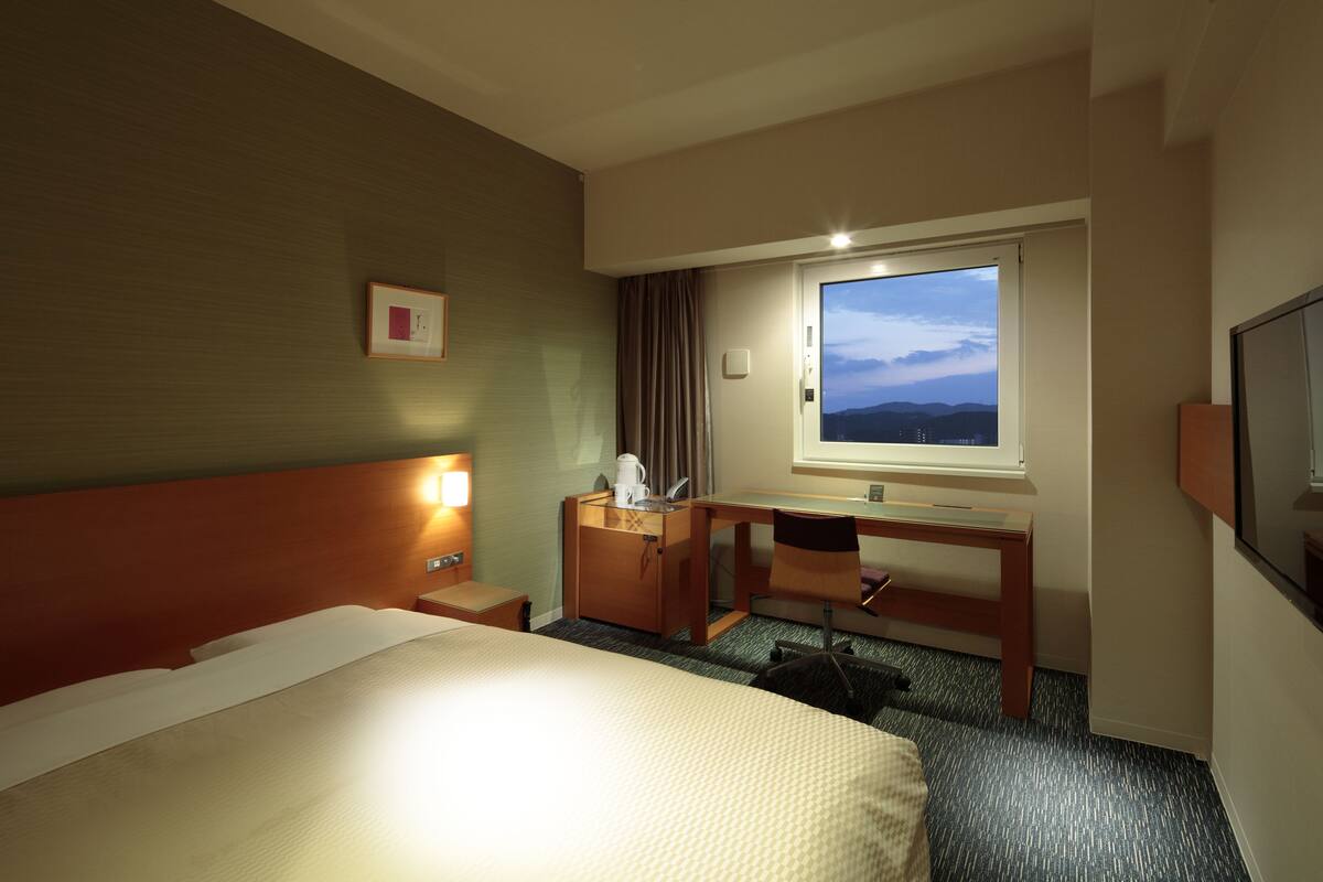 Een hotelkamer met een bed, bureau, stoel en een raam met uitzicht.