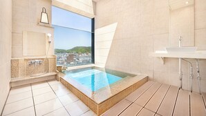 Un baño moderno con bañera de hidromasaje con cerramiento de vidrio, un ventanal con vistas a la ciudad y una zona de lavamanos independiente.