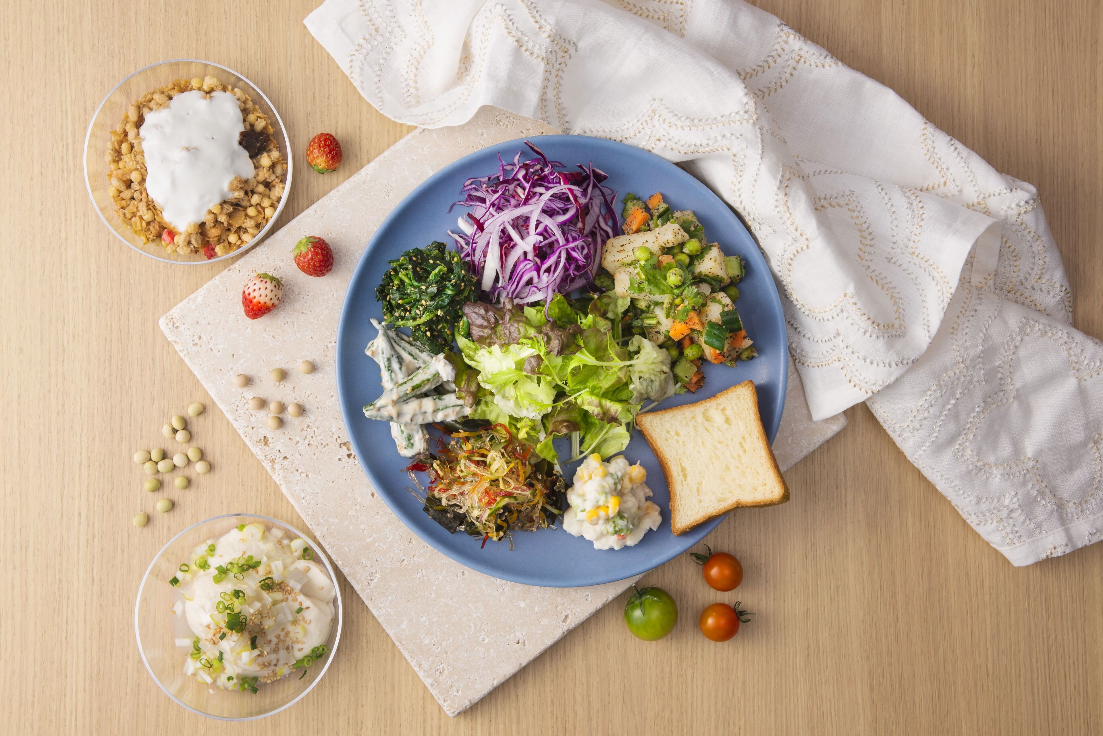 A plate with various salads, a slice of bread, and a small bowl of yogurt.