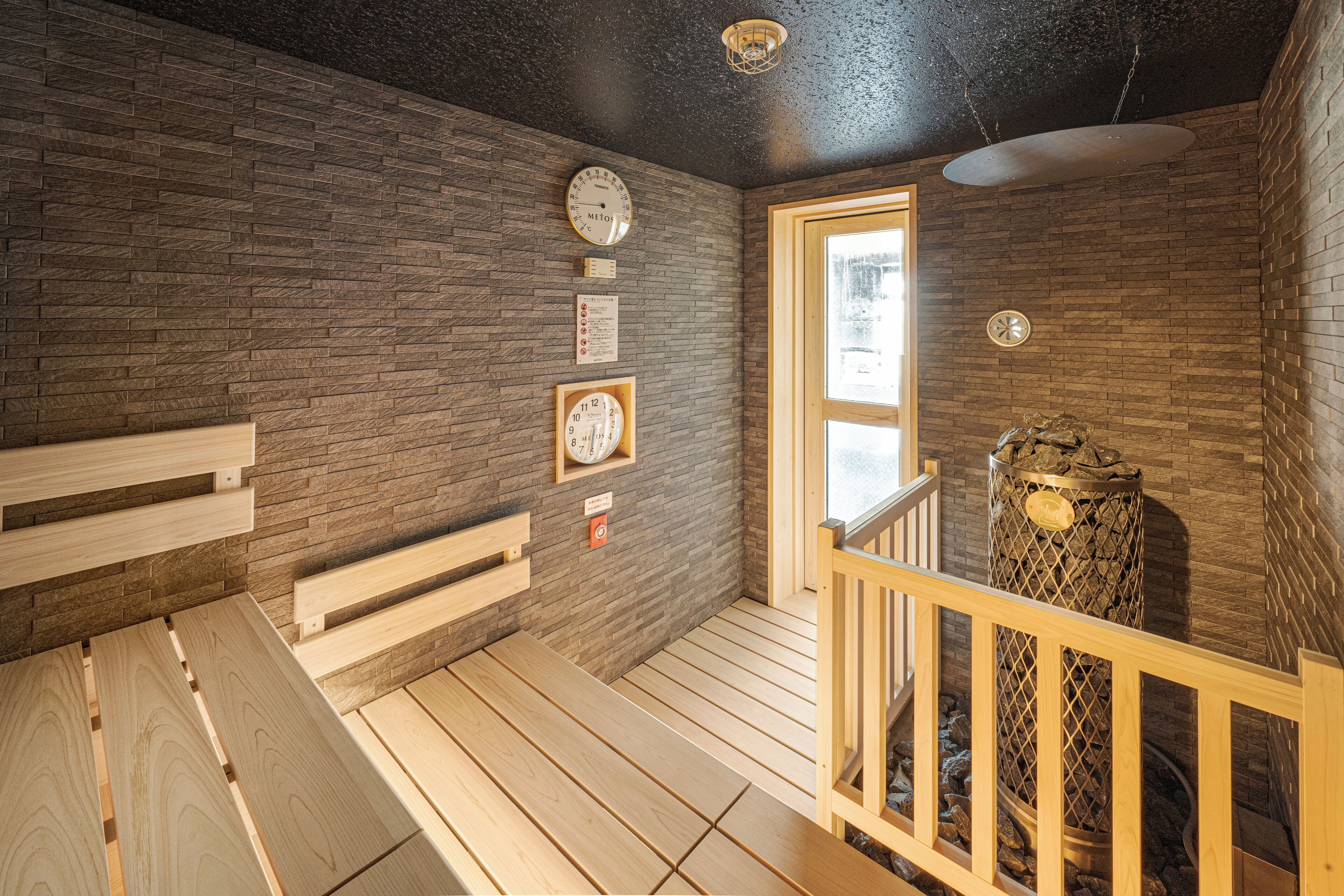 A sauna room with wooden benches, a wooden railing, and a stone wall.