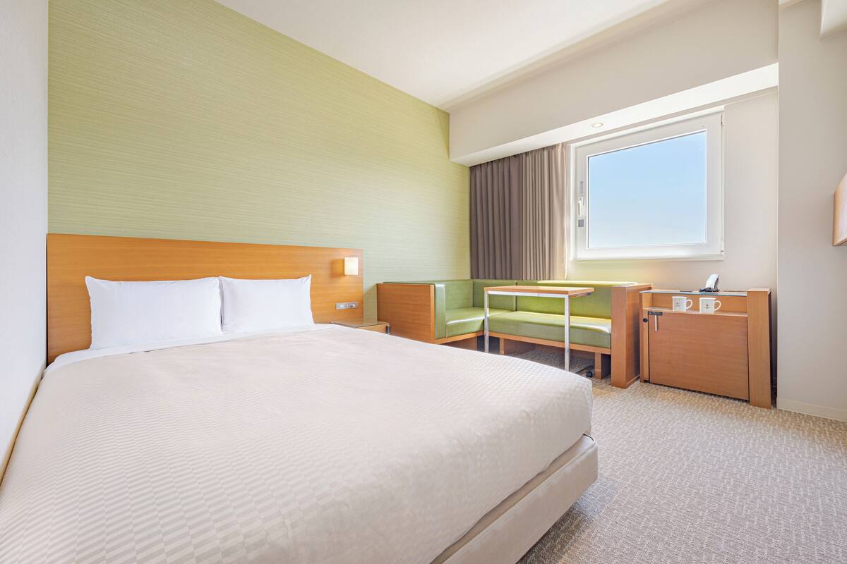 Een hotelkamer met een groot bed, een bureau, een stoel en een raam met gordijnen.