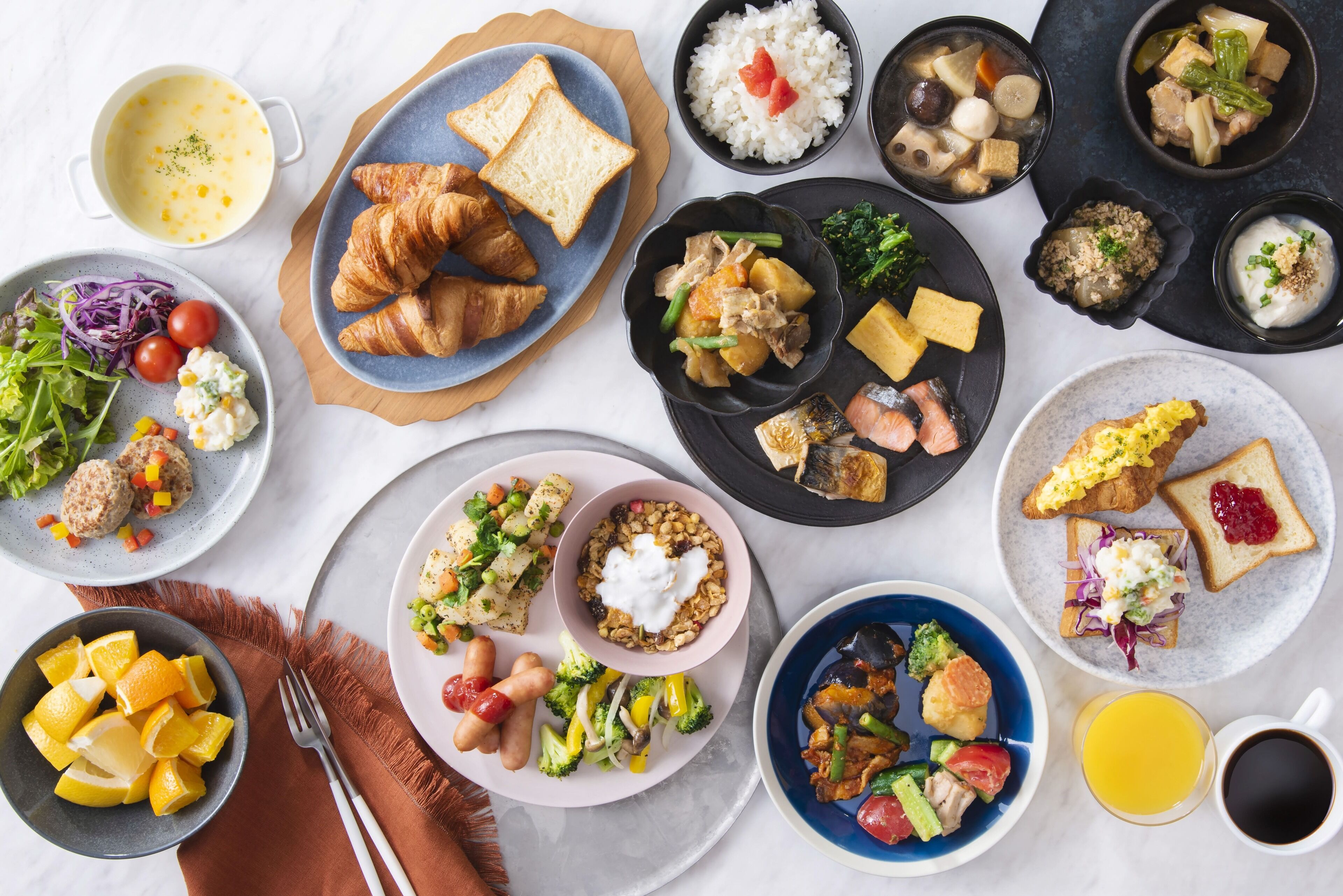 A variety of dishes including croissants, rice, and vegetables, arranged on multiple plates and bowls.