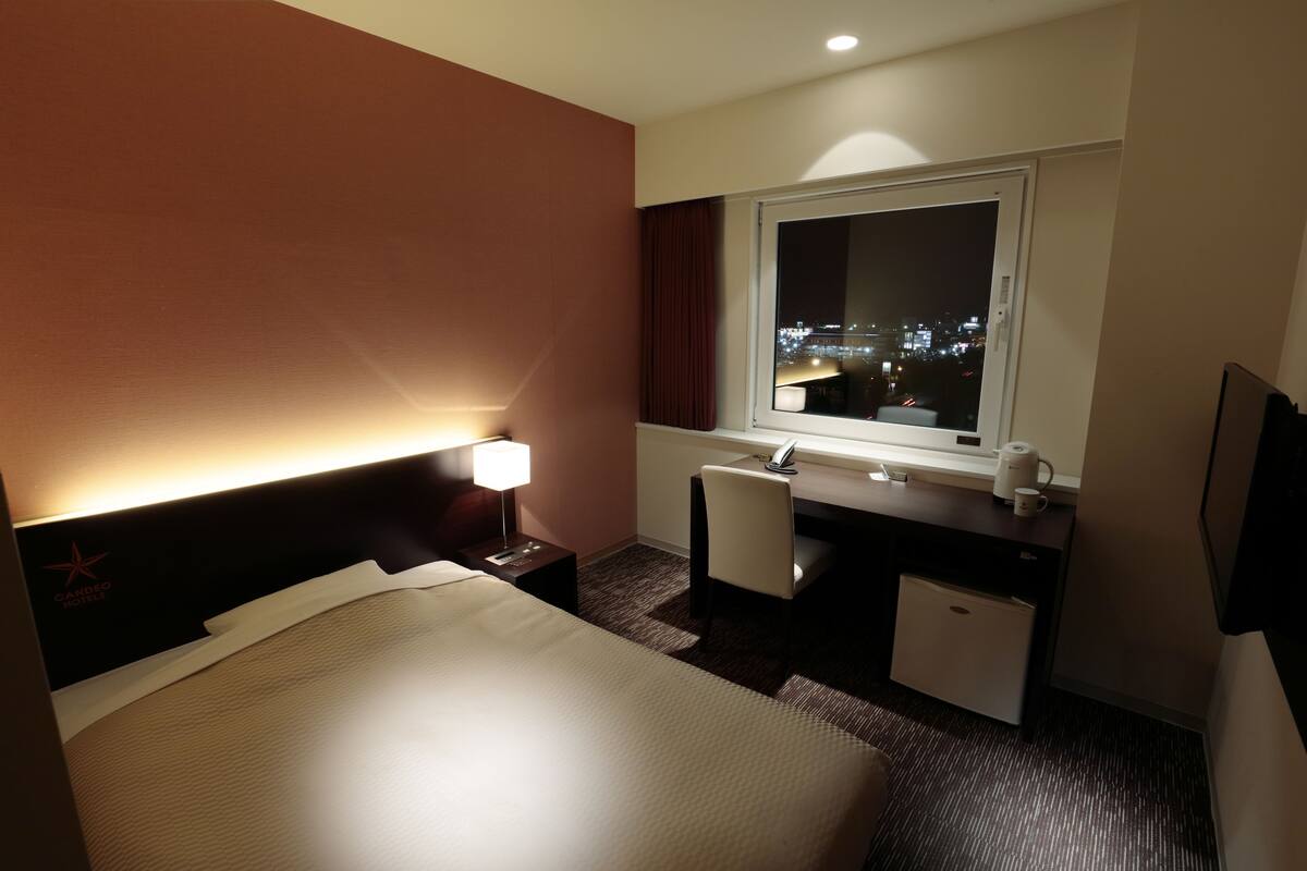 Habitación de hotel con cama, escritorio y ventana con vista a la ciudad de noche.
