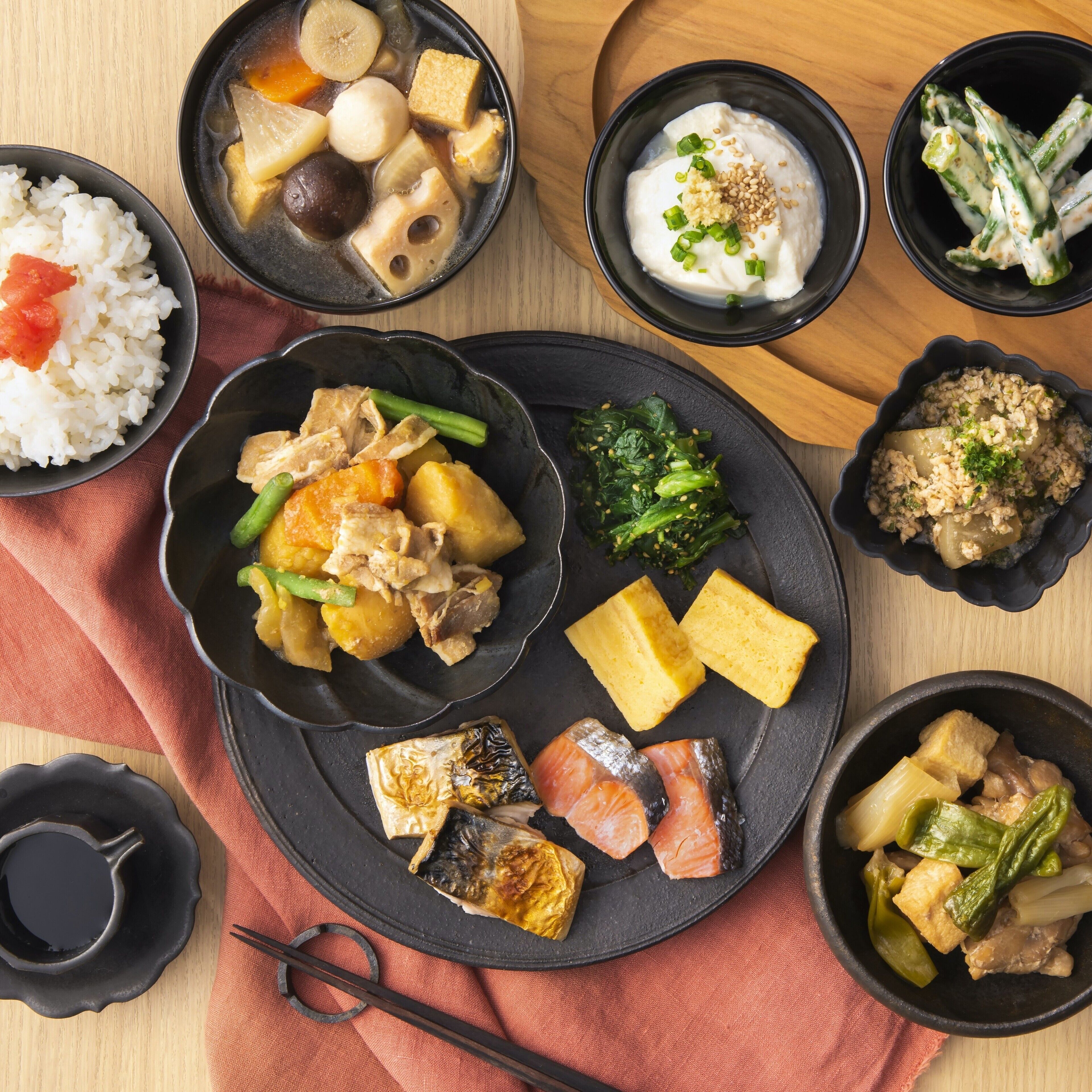 Variedad de platos que incluyen arroz, tofu, pescado y verduras servidos en cuencos negros sobre una mesa de madera.