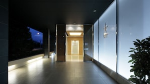 A modern hotel corridor with a glass wall on the right, a wooden door at the end, and a well-lit walkway. - Candeo Hotels Kumamoto Airport Kikuyo (Kikuyo)