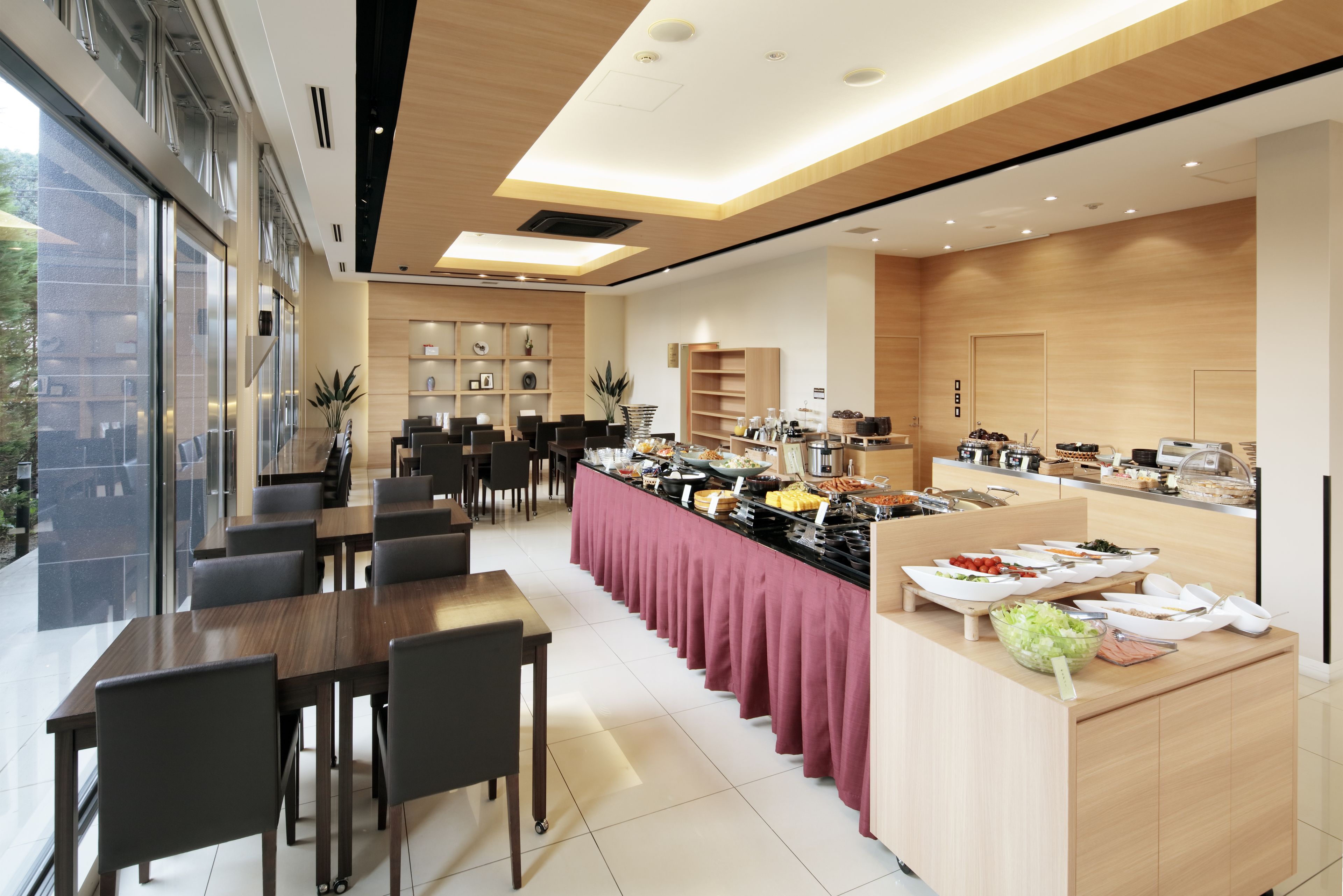 A modern dining area with a long table and chairs, a buffet station with various food items, and a reception desk.