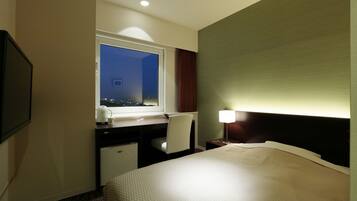 Habitación de hotel con cama, escritorio, silla y ventana con vista a la ciudad de noche.