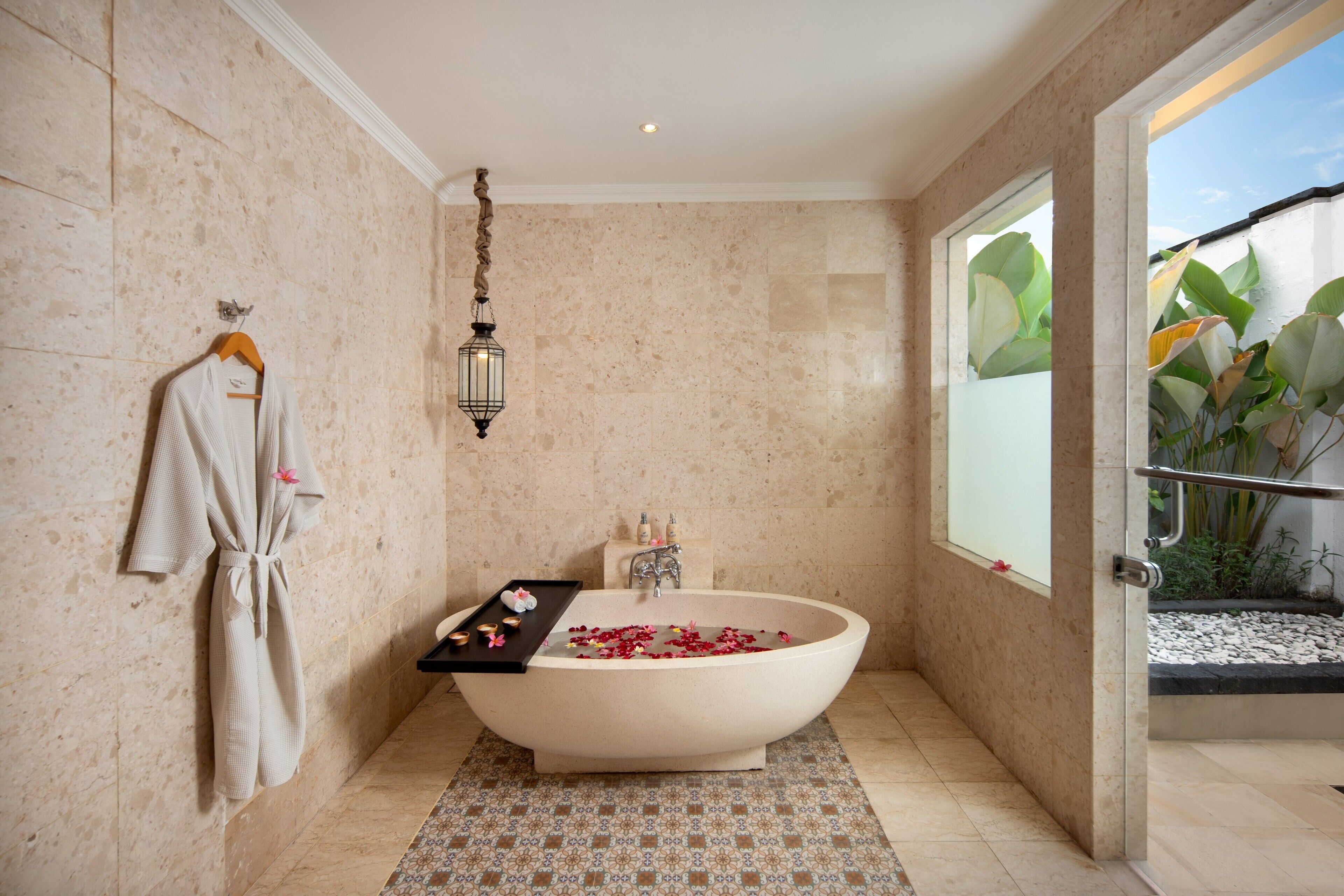 Une salle de bain avec une baignoire sur pieds, un porte-serviettes avec un peignoir, un plateau contenant des produits de bain et une fenêtre donnant sur un paysage verdoyant.
