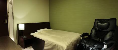 A hotel room with a bed, a massage chair, a nightstand with a lamp, and a wooden floor.