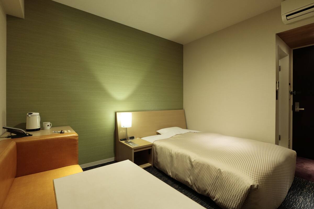 A hotel room with a bed, a bedside table with a lamp, a coffee maker, and a telephone.