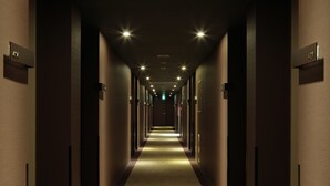 A long, narrow hotel corridor with a carpeted floor, recessed lighting, and doors on both sides.