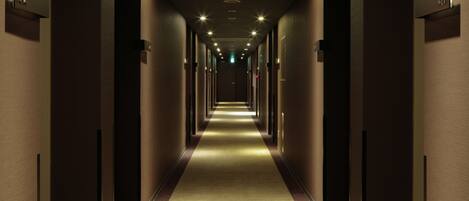 A long, narrow hotel corridor with a carpeted floor, recessed lighting, and doors on both sides.