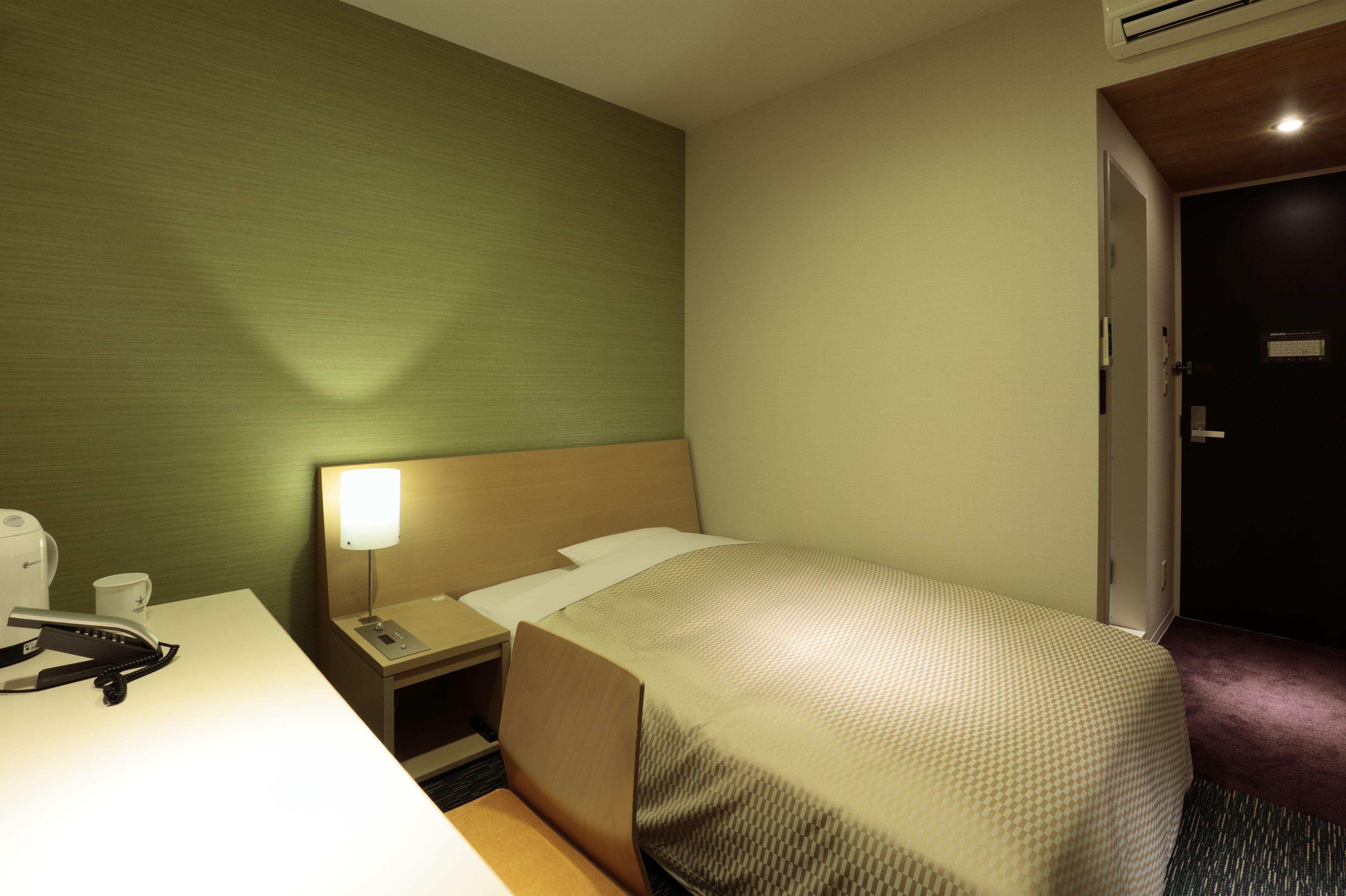 Une chambre d’hôtel avec un lit simple, une table de chevet avec une lampe, un téléphone et une machine à café.