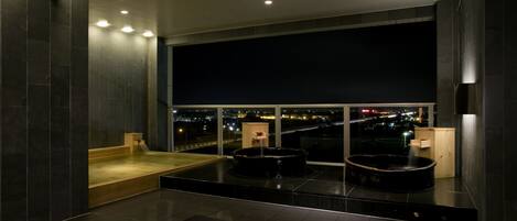 A modern bathroom with a large bathtub, a shower area, and a view of the city at night.