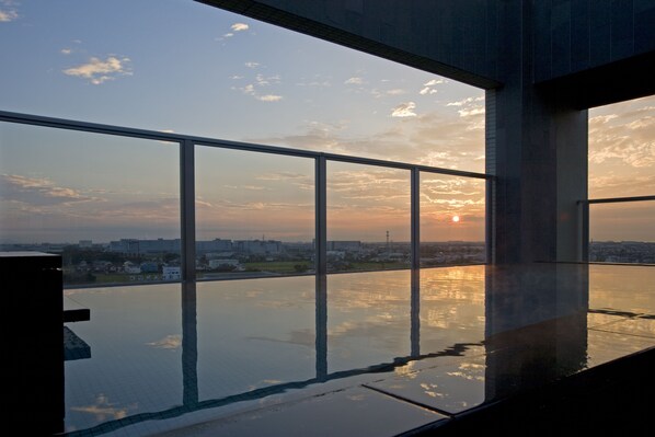 A modern building with large glass windows overlooking a cityscape at sunset.