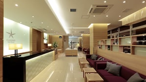 A hotel lobby with a reception desk, seating area, and a staircase leading to the upper floor.